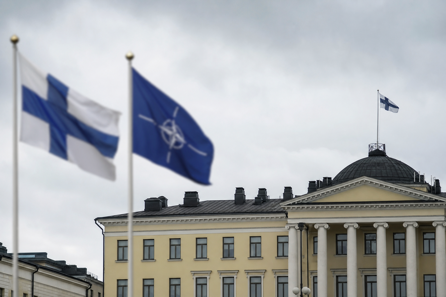 Suomen ja Naton liput valtionhallinnon rakennuksen edustalla pilvisenä päivänä.
