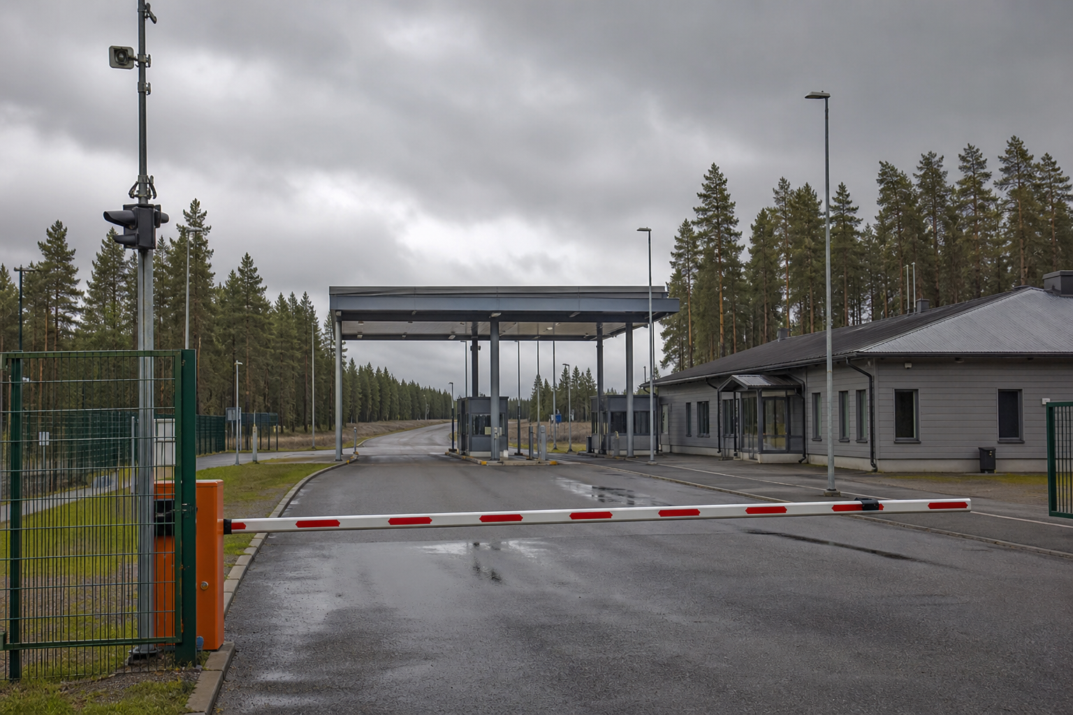 Suljettu rajapuomi tyhjällä tiellä metsäisellä rajanylityspaikalla pilvisessä säässä.