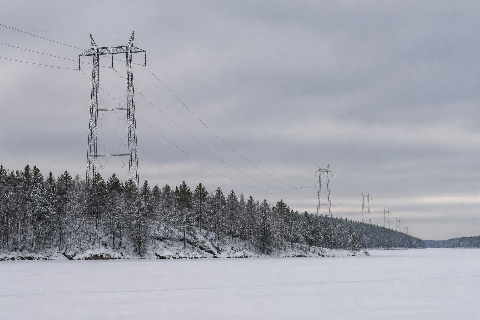 Lumisessa suomalaisessa maisemassa korkeajännitelinja kulkee jäätyneen järven yli harmaan talvitaivaan alla.