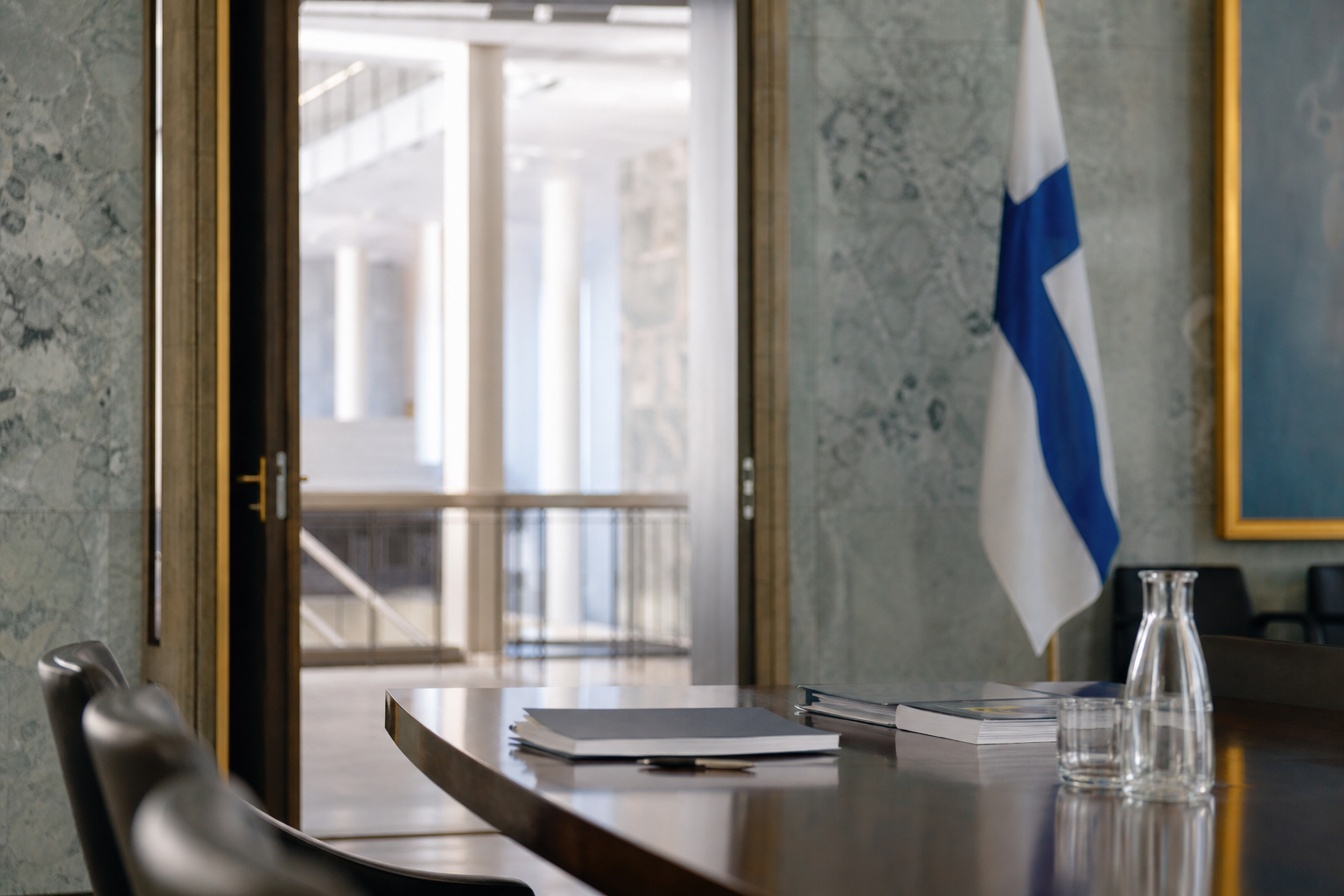 Moderni eduskunnan käytävätila, pöydällä asiakirjoja ja taustalla Suomen lippu.