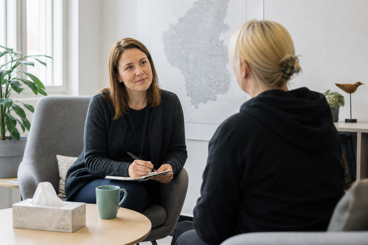 Sosiaalityöntekijä keskustelee asiakkaan kanssa valoisassa yhteisötilassa, symboloi kohtaavaa asiakastyötä.