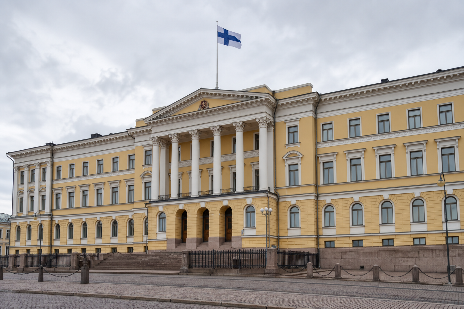 Suomen valtioneuvoston linna Helsingissä, sinivalkoinen lippu liehuu katolla, pilvinen taivas.