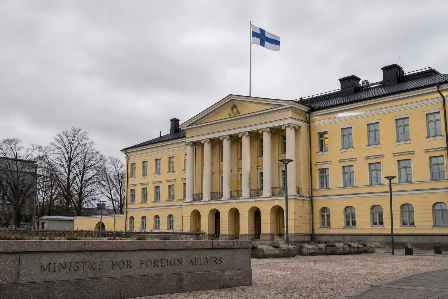 Suomen ulkoministeriön rakennus Helsingissä pilvisenä päivänä, lipputanko ja Suomen lippu.