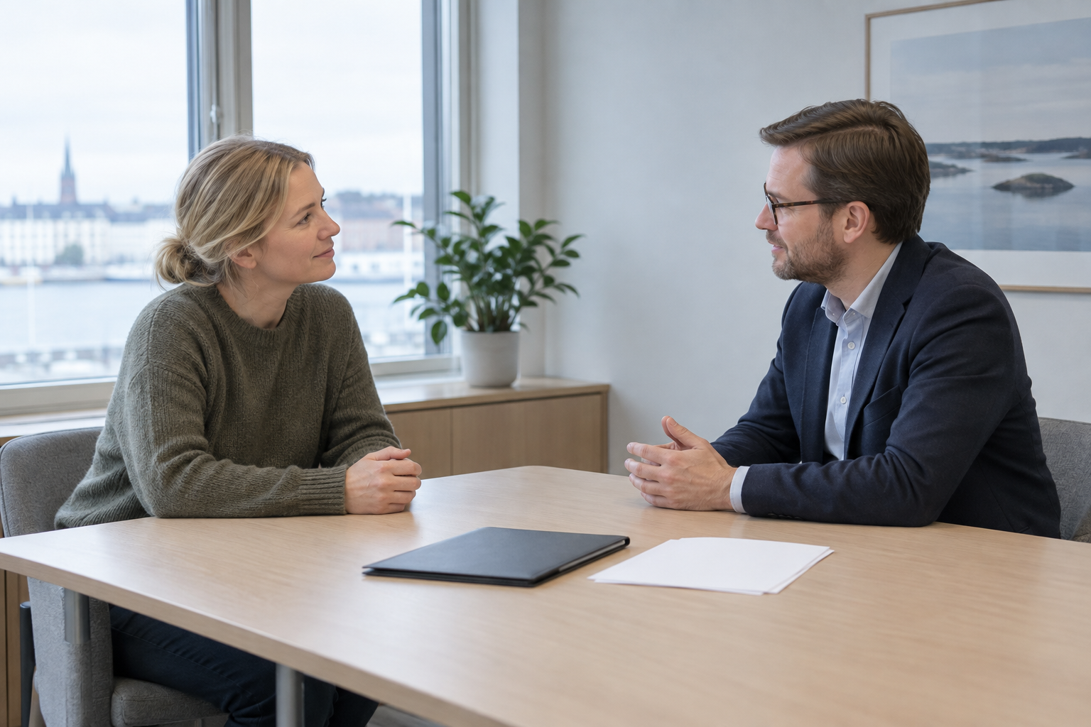 Pienyrittäjä ja pankkineuvoja keskustelevat pöydän ääressä. Pöydällä on kansio ja tyhjiä paperiarkkeja.